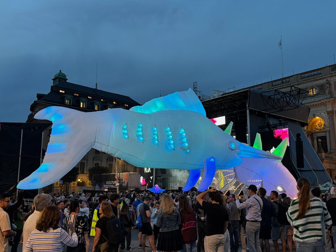 Close view of a glowing blue and white fish lantern above the festival crowd at dusk