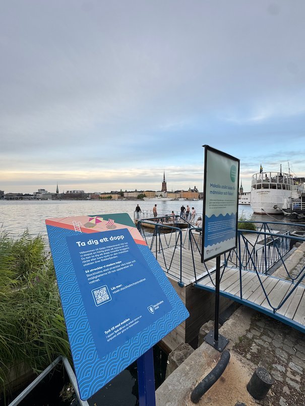 Information signs on a jetty by the water, with Gamla stan and Riddarholmen in the background