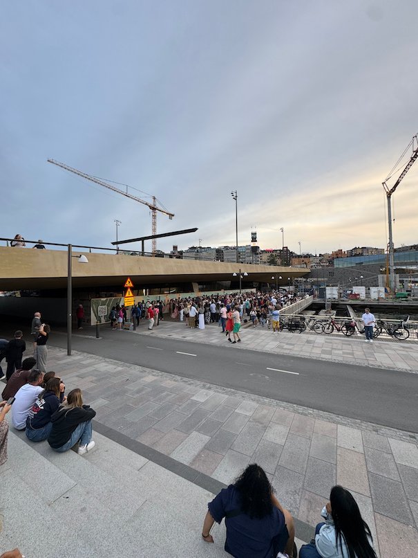 People sit on wide stone steps by the water at Slussen on a summer evening