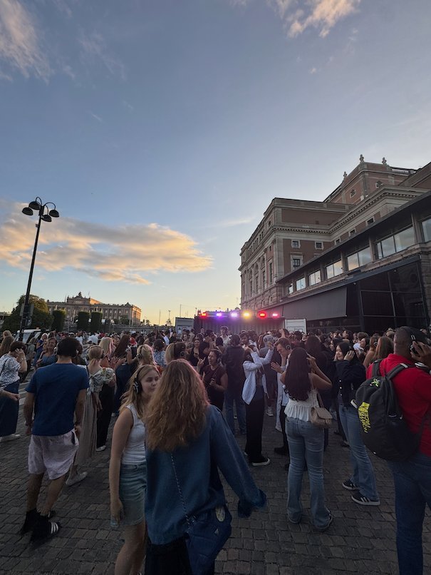 Festival visitors in front of a stage by a large stone building at sunset