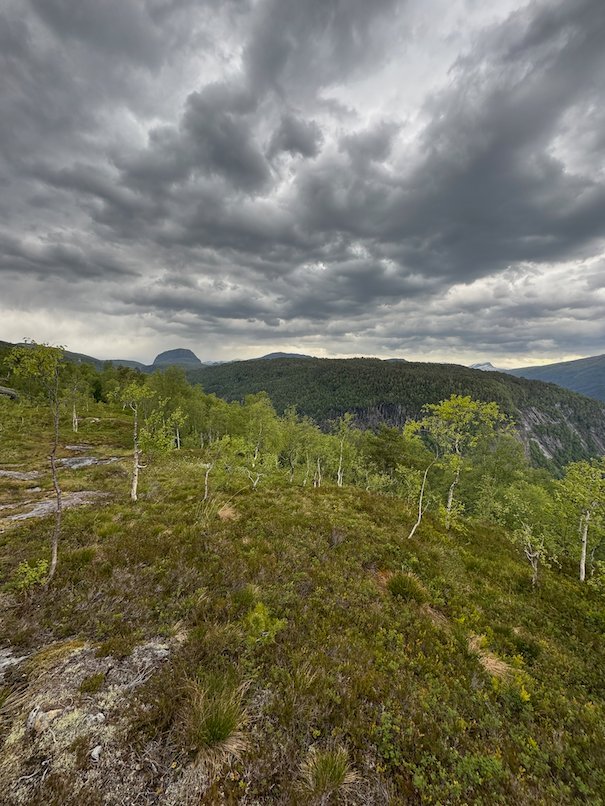 Mountains behind a green hillside under a cloudy sky