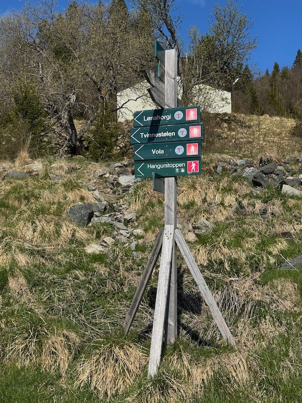 Signpost to Lønahorgi, Vola and Hangurstoppen on a grassy slope near a cabin