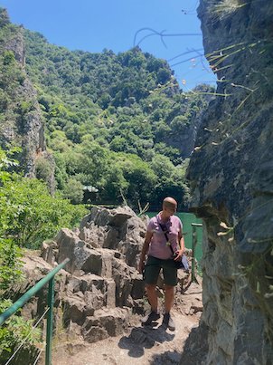 A traveler stands on a rocky path below a cliff at Matka Canyon near Skopje.