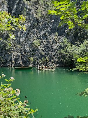Small boats float on the green lake below a rock wall in Matka Canyon.