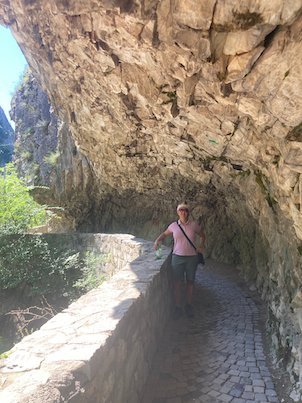 A traveler walks on a stone path under an overhanging rock at Matka Canyon.