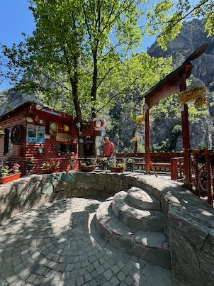 A red wooden restaurant and a stone terrace stand under trees in Matka Canyon.