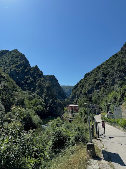 A road runs beside the river between steep green mountains at Matka Canyon.