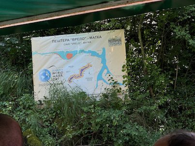 The Vrelo Cave sign stands among bushes, seen from a boat in Matka Canyon.