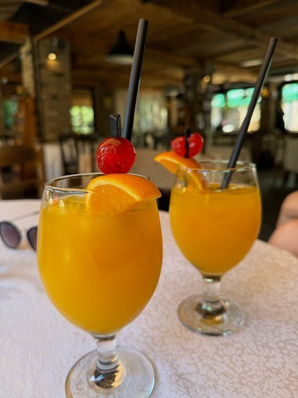 Two glasses of orange juice with fruit and straws stand on a restaurant table at Matka.