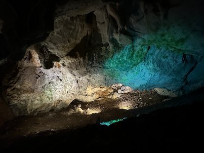 Green light shines on a rock wall above dark water in Vrelo Cave at Matka.