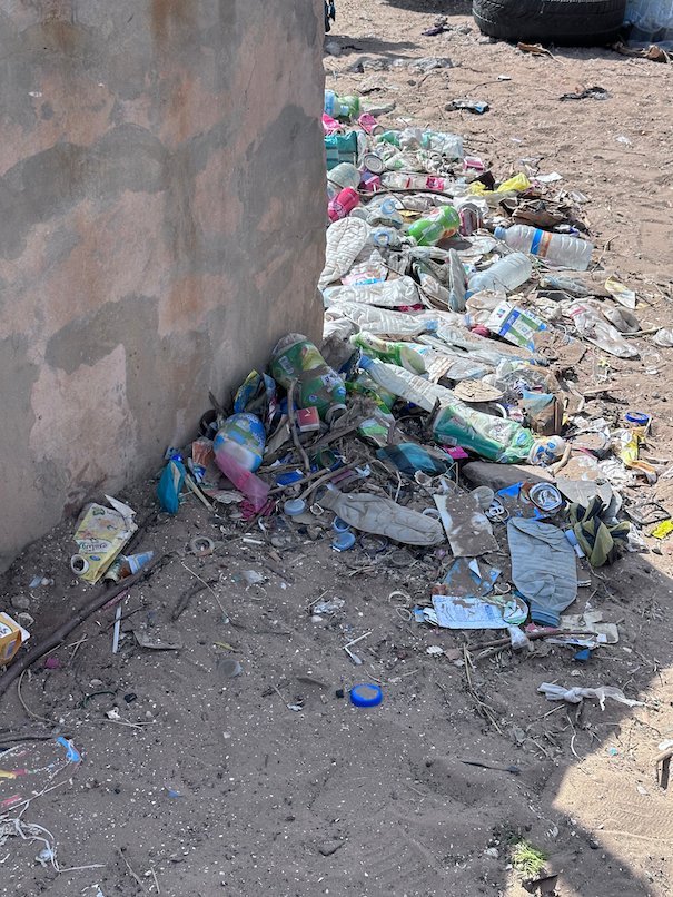 Plastic bottles and garbage pile up next to a wall.