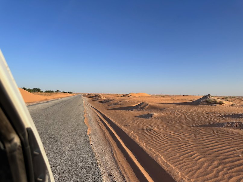 Orange sand dunes reach the edge of the road.