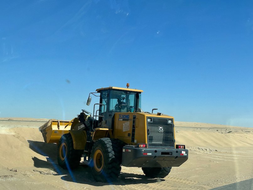 A yellow wheel loader clears sand from the road.