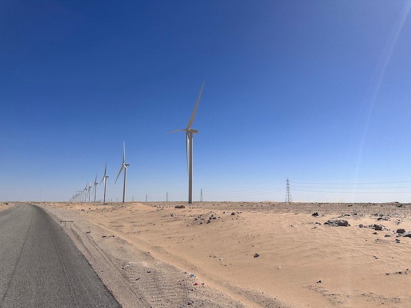 Wind turbines stand in a row next to a desert road.