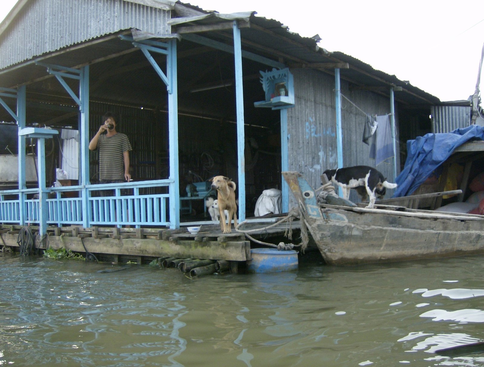 A man stands on the porch of a blue floating house on the river in the Mekong Delta.