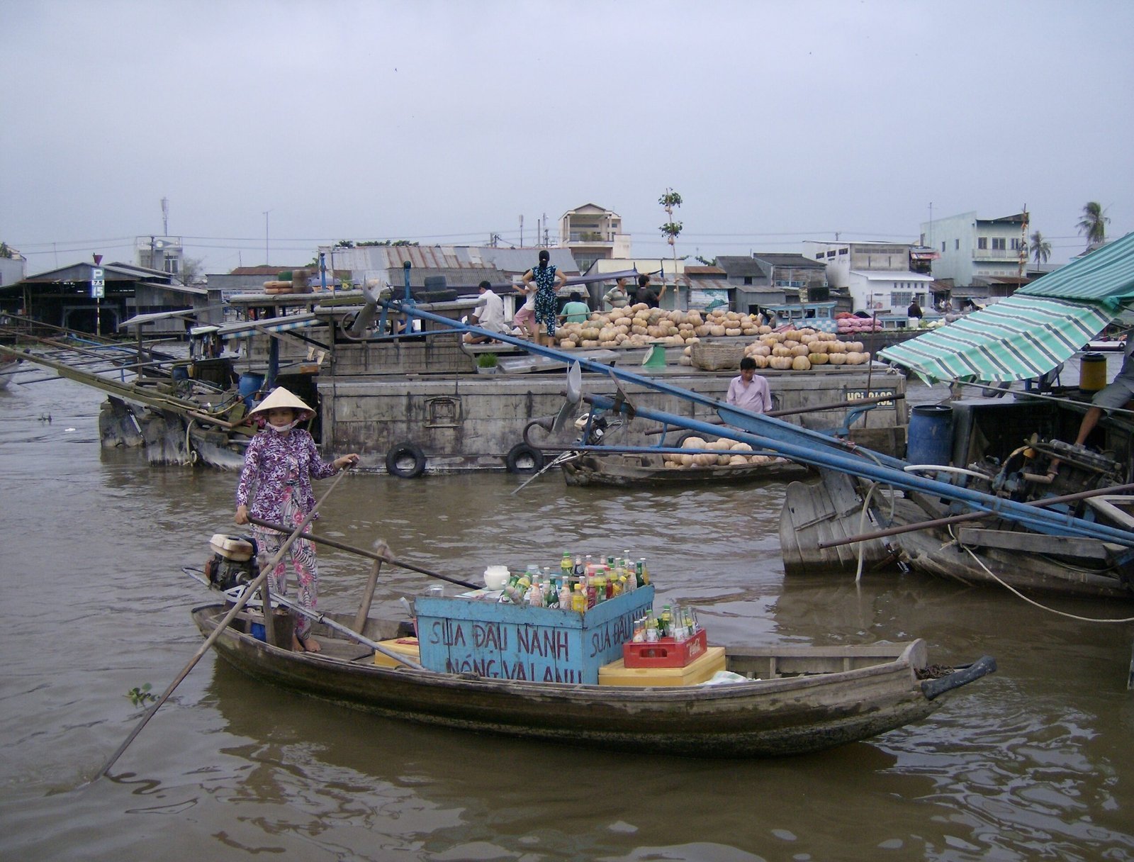 A woman in a conical hat rows a small boat at a floating market in the Mekong Delta.