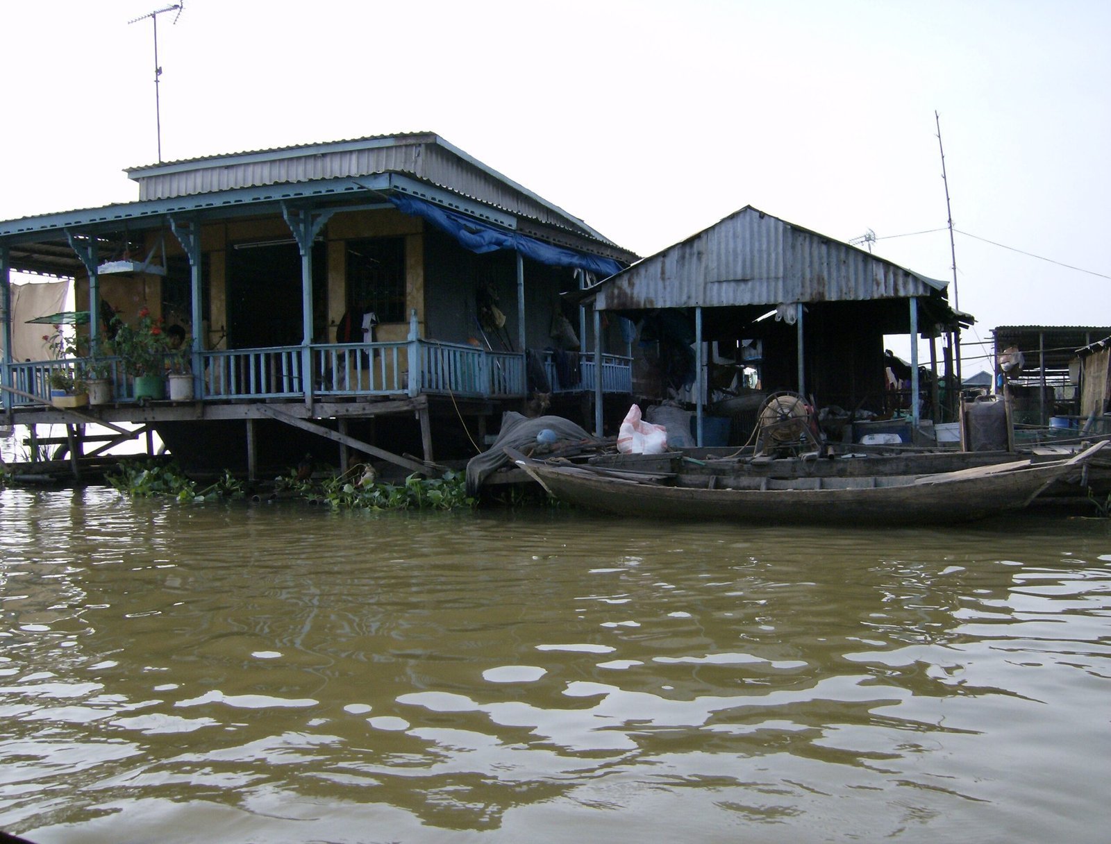 A blue wooden house on stilts stands over the brown river in the Mekong Delta.