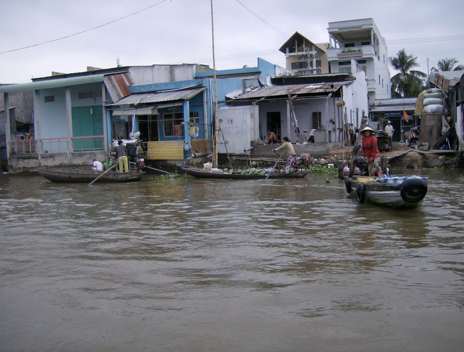 Small boats pass colorful riverside houses on a river in the Mekong Delta.