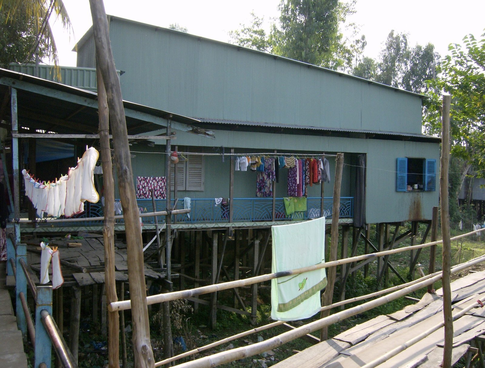 Laundry hangs on a stilt house next to a wooden walkway in the Mekong Delta.