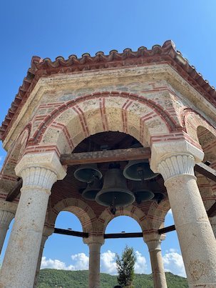 Bell pavilion with arches and columns under a blue sky at a Meteora monastery