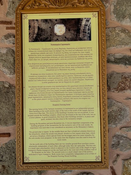 History panel in a gold frame on a stone wall at a Meteora monastery