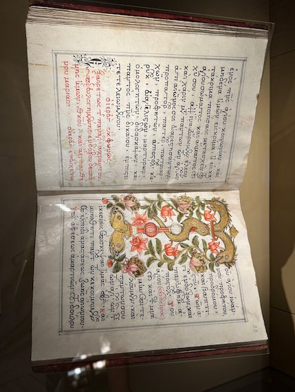 Open old book with handwritten text and a painted flower pattern in a Meteora monastery