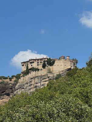 Long monastery building on top of a rock at Meteora, with white clouds