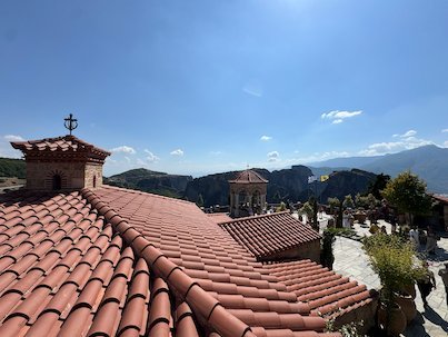 Red tile roofs and a cross of a Meteora monastery, with mountains behind
