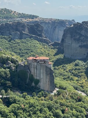 Monastery on a single rock above a green forest, with high cliffs behind