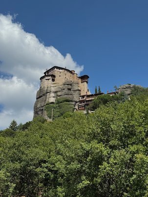 Monastery on a tall rock above green trees at Meteora