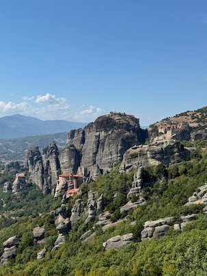 Rock towers and a monastery above a wide green valley at Meteora