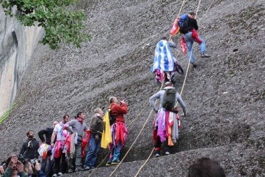 People climb a steep rock with ropes to bring cloths to a cave at Meteora