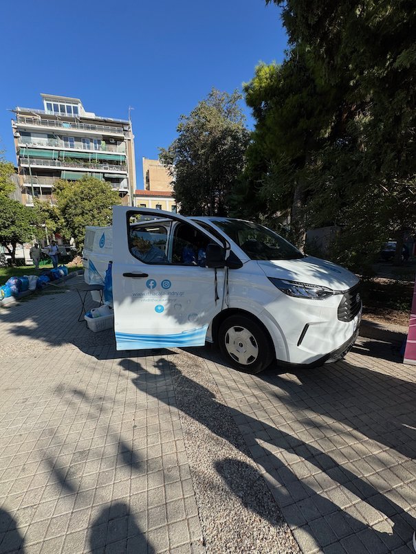 White mobile laundry van with open doors in a park in Athens