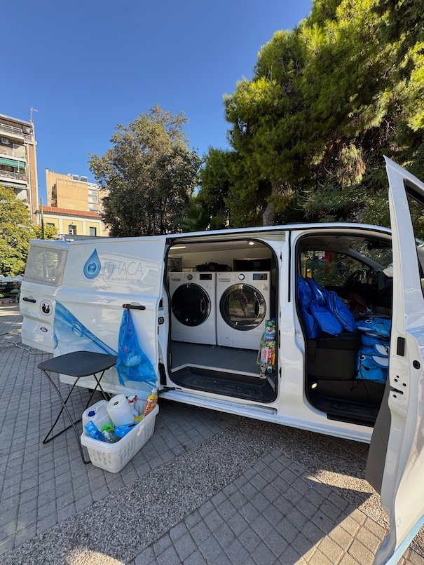 Side door of a van with two washing machines and bags of supplies, parked in Athens