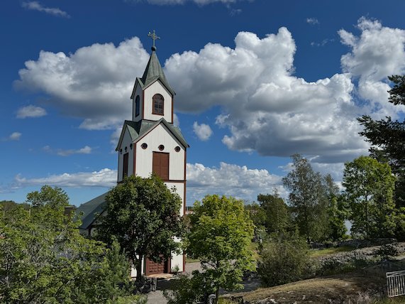 White wooden church with a tall tower on Möja, under a blue summer sky with white clouds