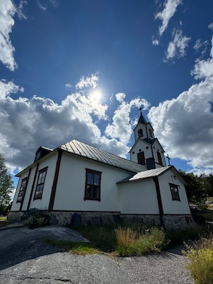 Side view of the white wooden church on Möja, with the sun behind the tower and bare rock in front