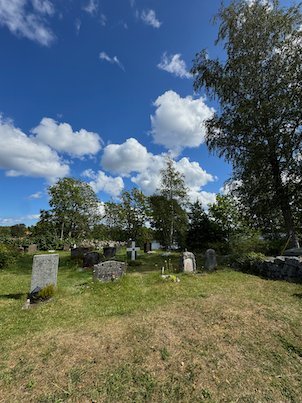 Old gravestones in the grass of Möja churchyard, with birch trees and blue sky