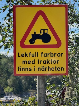 Yellow Swedish road sign with a tractor and the text Lekfull farbror med traktor finns i närheten, a joke sign on Möja