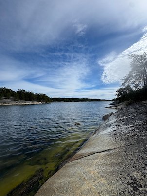 Smooth granite slab that slopes into calm water, under a blue sky with clouds