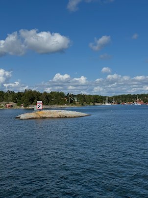 Small rock with a navigation sign in a harbour bay, houses and boats behind