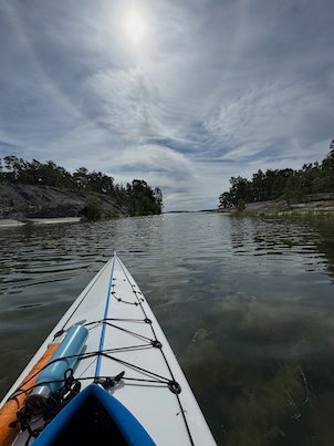 Kayak bow on still water between two rocky islands, sun behind thin clouds