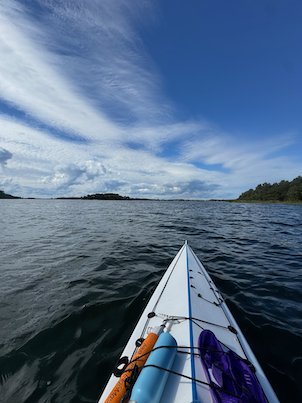 White kayak bow pointing to open water and distant islands under streaky clouds