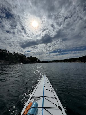 Kayak bow on dark water, with the sun behind grey clouds
