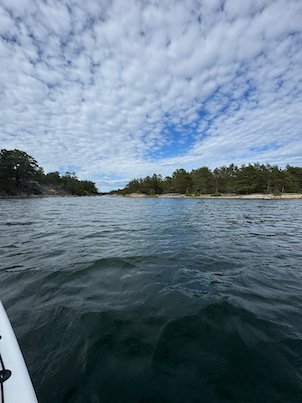 Calm water and low wooded islands under a cloudy sky, seen from a kayak