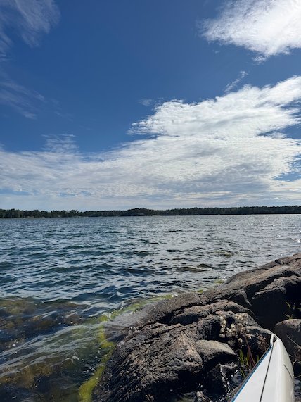 Kayak beside a dark rock with green seaweed, open water behind