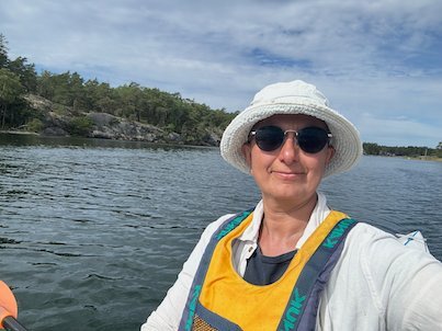 Selfie in a kayak with sunglasses and a white sun hat, rocky shore behind