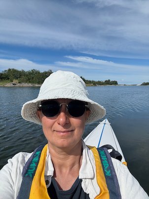 Selfie with a white sun hat and sunglasses, kayak and calm water behind