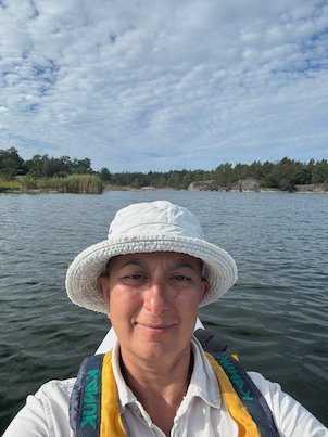 Selfie in a kayak with a white sun hat and a yellow life jacket, islands behind