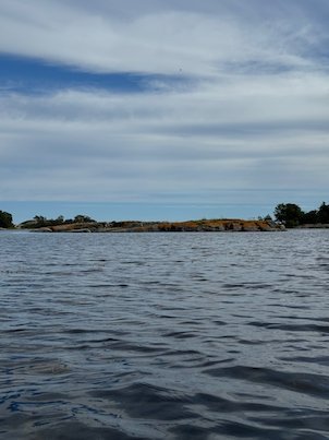 Low island with reddish rocks on the horizon, under a grey and blue sky