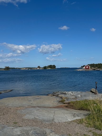 Rocky shore and a red cottage on a point, with blue sea and small islands